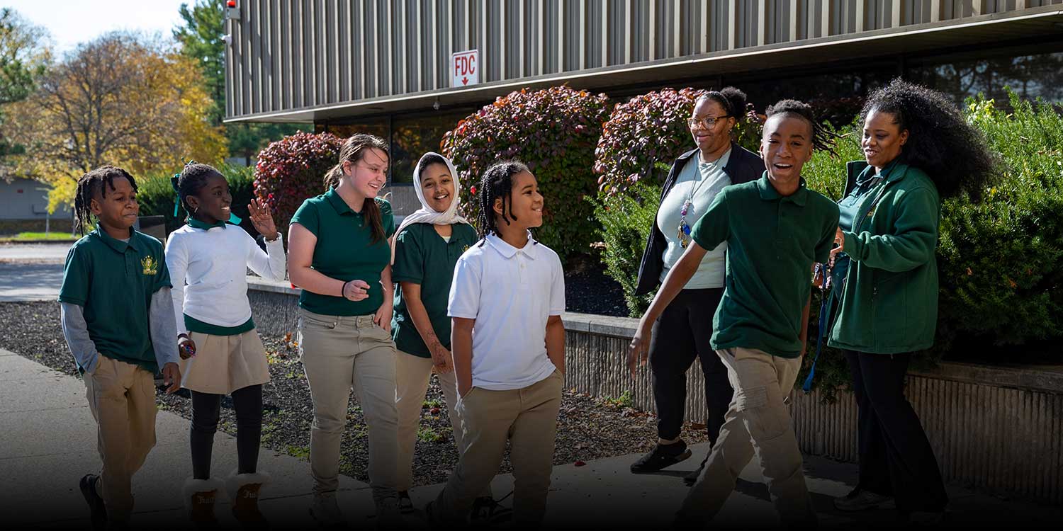 Sagewood students in green and white uniforms walking outside the school with staff.
